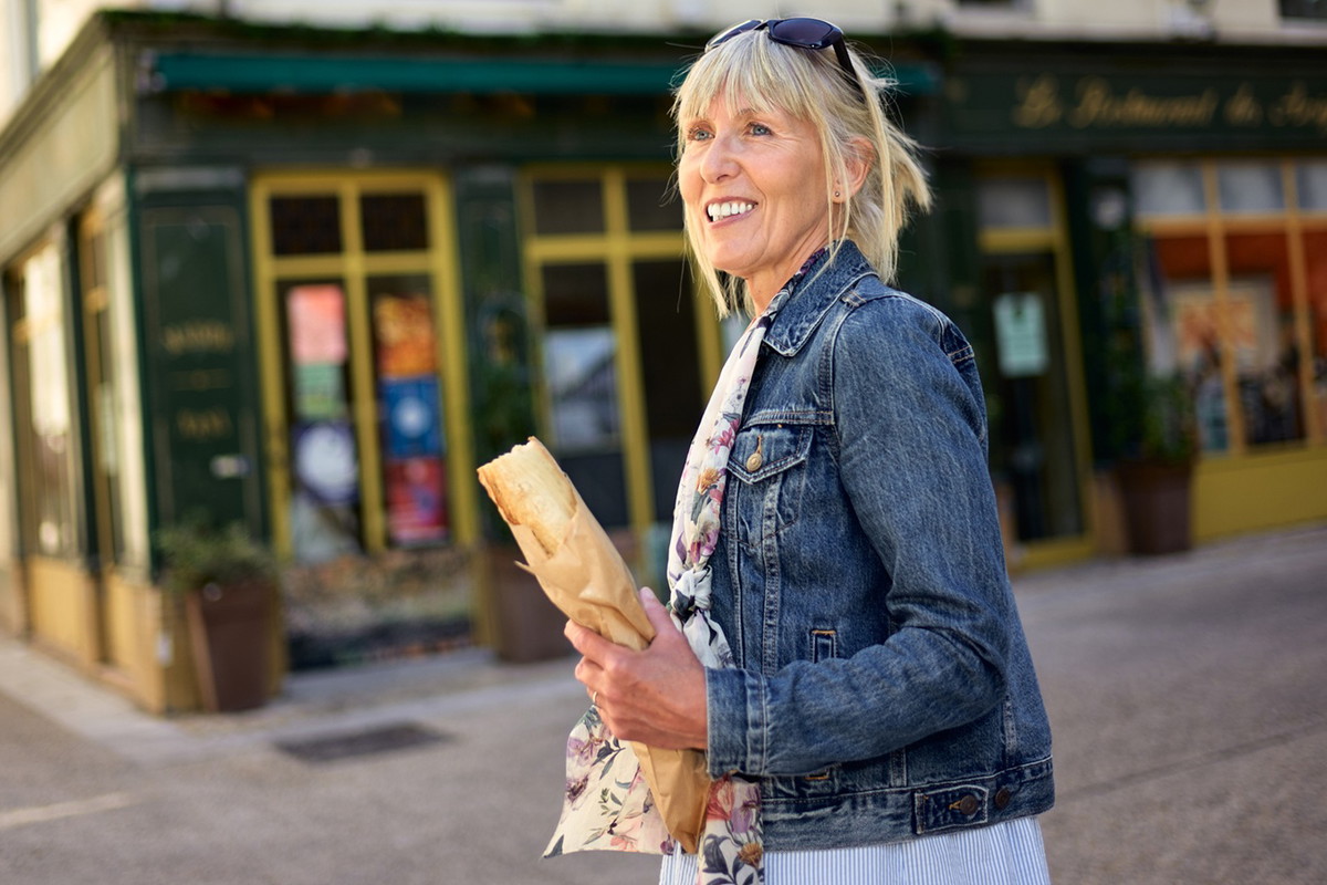 kobieta w wieku 50 plus blondynka w jeansowej kurtce stoi w Avignon w Prowansji we Francji z bagietką i uśmiecha się