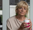 kobieta w wieku 65 plus blondynka siedzi w kuchni z kubkiem w ręce zamyślona i smutna