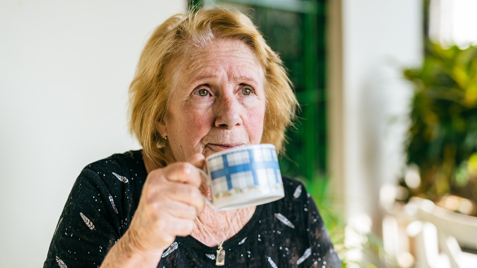 kobieta w wieku 70 plus siedzi przy stole w kuchni i pije herbatę zamyślona i smutna