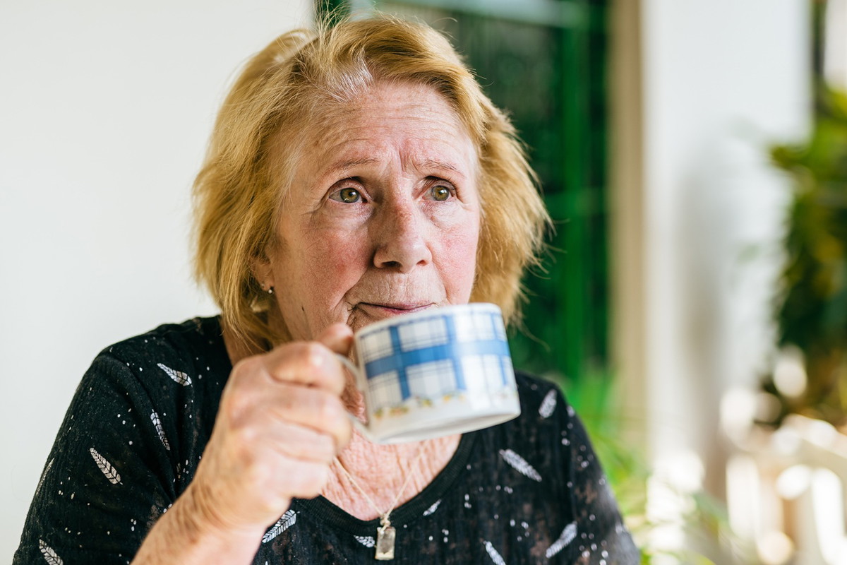 kobieta w wieku 70 plus siedzi przy stole w kuchni i pije herbatę zamyślona i smutna
