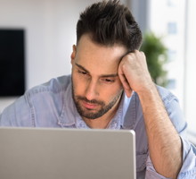 mężczyzna w wieku 30 plus w jeansowej koszuli siedzi przy laptopie załamany