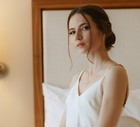 młoda dziewczyna w białej jedwabnej sukience siedzi w pokoju z zamyśloną i poważną miną