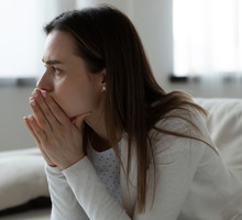 młoda kobieta w wieku 25 plus w białym sweterku siedzi na kanapie załamana