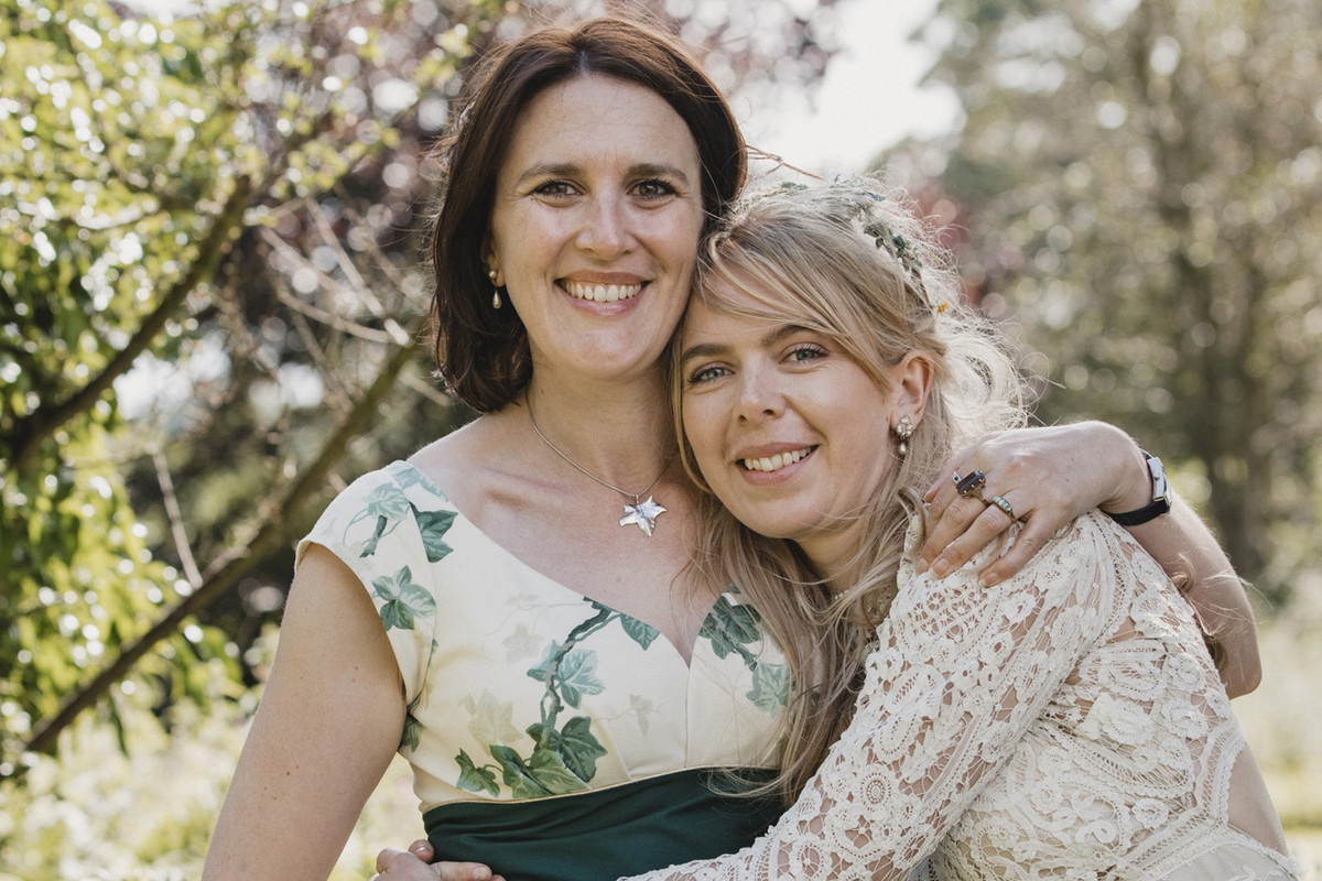 kobieta w wieku 50 plus stoi w ogrodzie z córką w suknie ślubnej w stylu boho i uśmiechają się obie