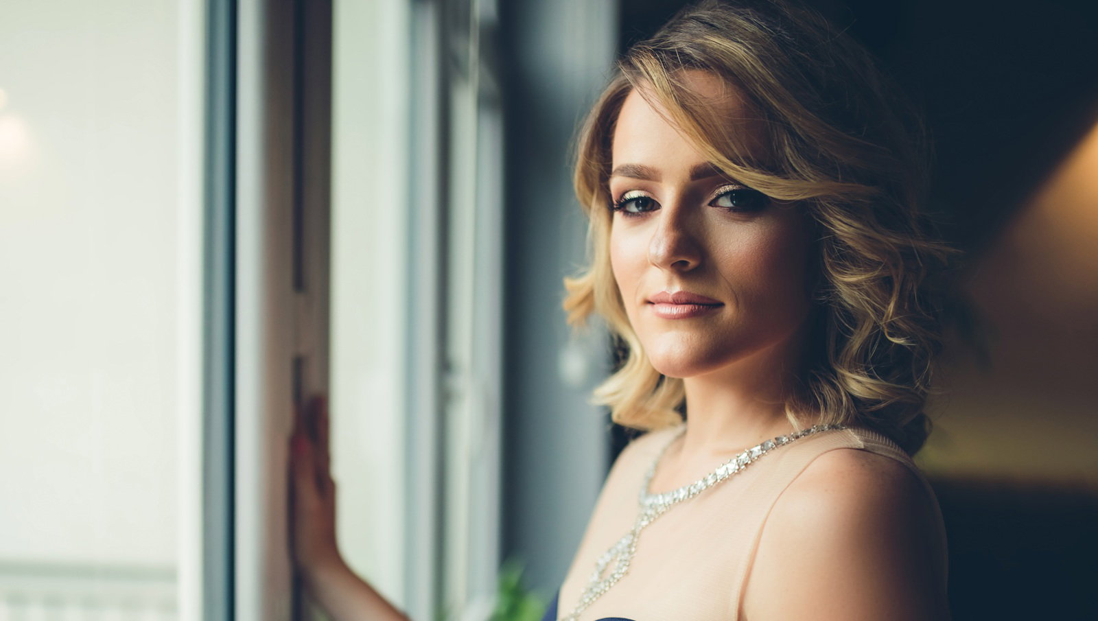 kobieta w wieku 30 plus w eleganckije sukni blondynka stoi przy oknie smutna i zamyślona