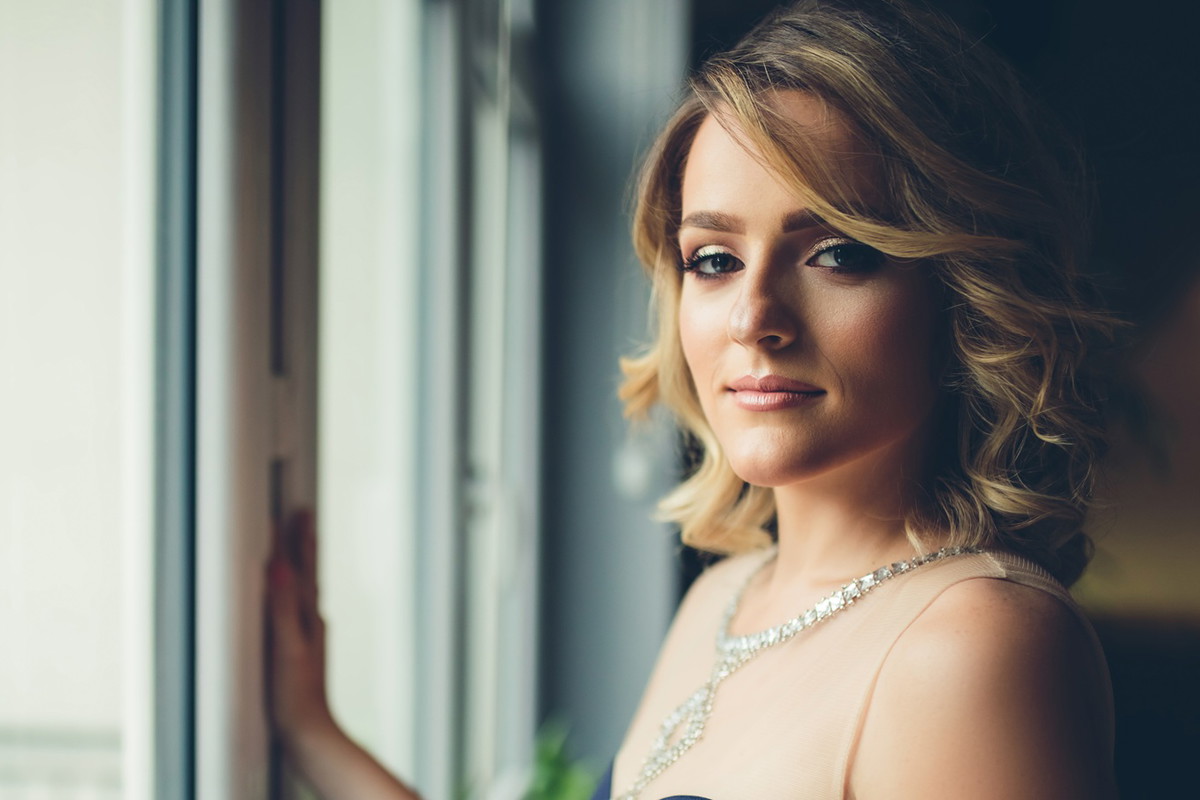 kobieta w wieku 30 plus w eleganckije sukni blondynka stoi przy oknie smutna i zamyślona