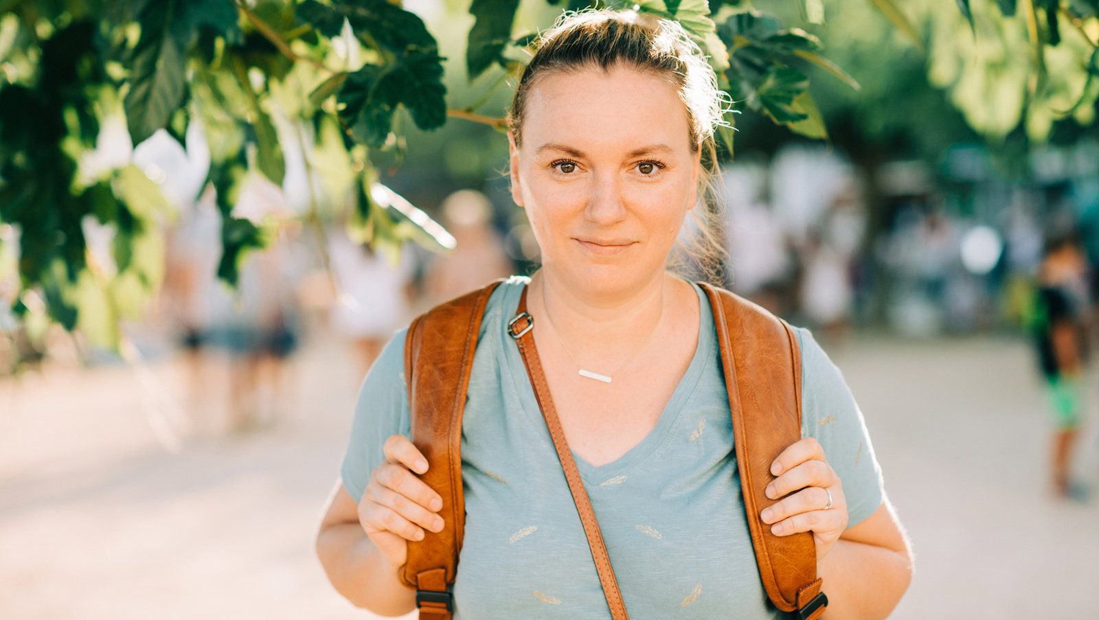 kobieta w wieku 30 plus w t-shircie z plecakiem stoi na ulicy i lekko się uśmiecha zadowolona
