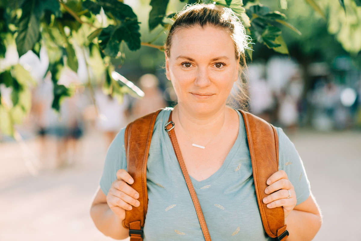 kobieta w wieku 30 plus w t-shircie z plecakiem stoi na ulicy i lekko się uśmiecha zadowolona