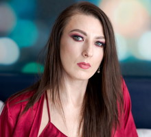 kobieta w wieku 30 plus z długimi włosami i w czerwonym szlafroku siedzi w pomieszczeniu z poważną miną