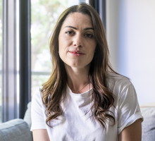 kobieta w wieku 35 plus w białym t-shircie siedzi na kanapie na tle okna z dumną miną