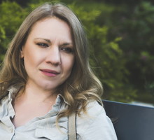 kobieta w wieku 40 plus siedzi na ławce na tle zieleni z plecakiem na plecach zamyślona