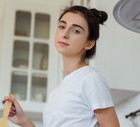 kobieta w wieku 30 plus w jansym t-shircie stoi w kuchni zamyślona z lekkim uśmiechem i patelnią w ręku