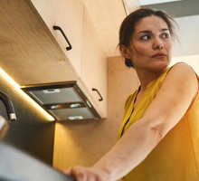 kobieta w wieku 30 plus z ciemnymi włosami stoi w kuchni zdenerwowana i załamana patrzy w dal na kogoś