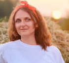 kobieta w wieku 35 plus z chusteczką na głowie i w białej bluzce stoi na tle zachodzącego słońca i siana