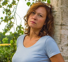 kobieta w wieku 50 plus w niebieskim t-shircie stoi przy brzozie zamyślona i smutna