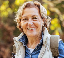 kobieta w wieku 60 plus w jeansowej koszuli na spacerze z plecakiem stoi uśmiechnięta