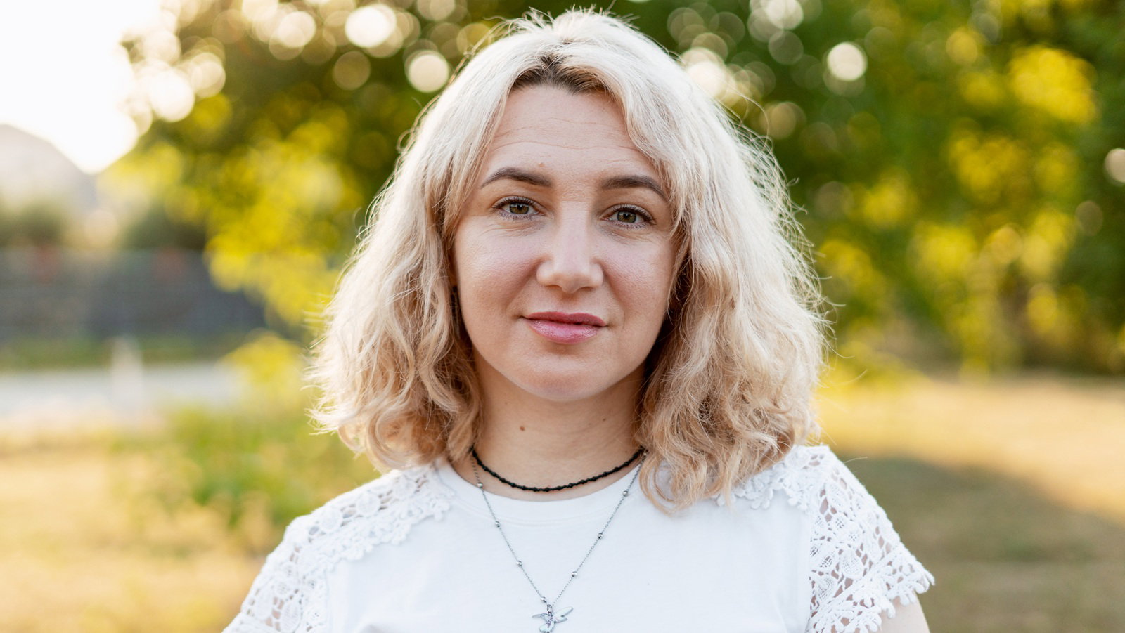 kobieta w wieku 30 plus blondynka w białej bluzce stoi na zewnątrz z lekko zdzwioną miną