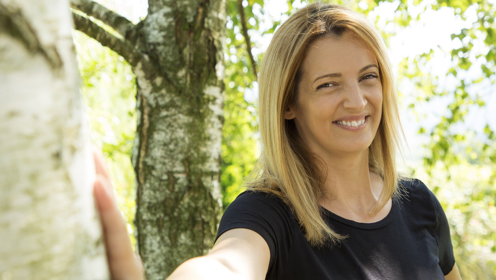 kobieta w wieku 30 plus blondynka z długimi włosami w czarnej koszulce stoi w brzeźniaku i się śmieje