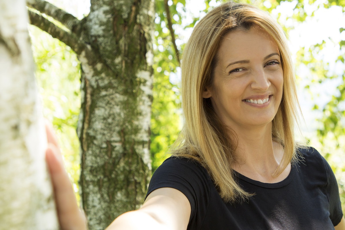 kobieta w wieku 30 plus blondynka z długimi włosami w czarnej koszulce stoi w brzeźniaku i się śmieje