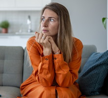 kobieta w wieku 30 plus w pomarańczowej sukience siedzi na kanapie zamyślona