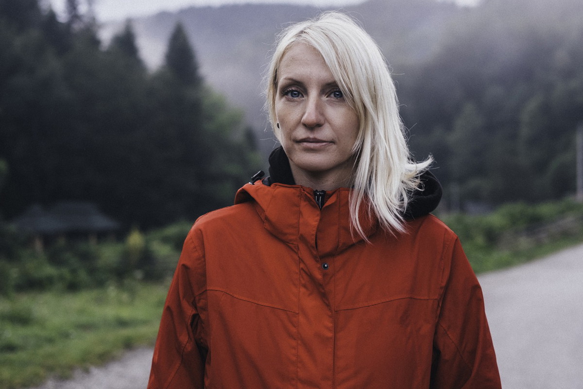 kobieta w wieku 35 plys blondynka w czerwnej kurtce stoi na tle gór zamyślona i załamana