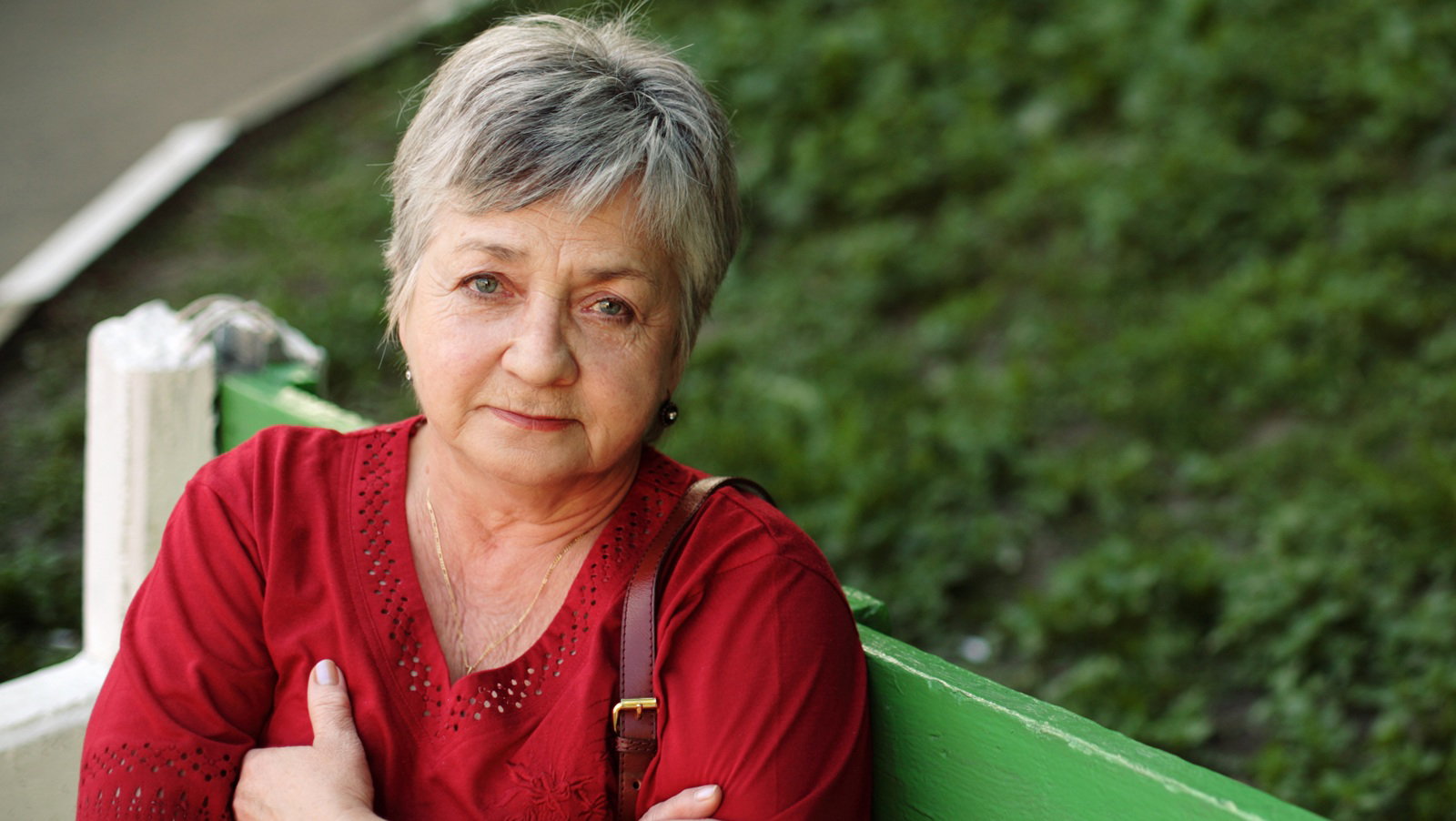 kobieta w wieku 55 plus z krótkimi włosami siedzi na ławce z torebką na ramieniu zasmucona