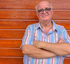 mężczyzna w wieku 60 plus w okularach łysiejący stoi na tle drewnianej ściany ze zmieszaną miną