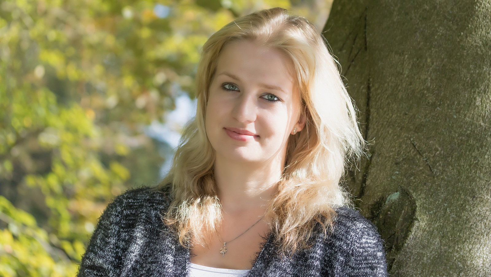 kobieta w wieku 30 plus blindynka stoi na zewnątrz na tle jesiennej roślinności z lekkim uśmiechem