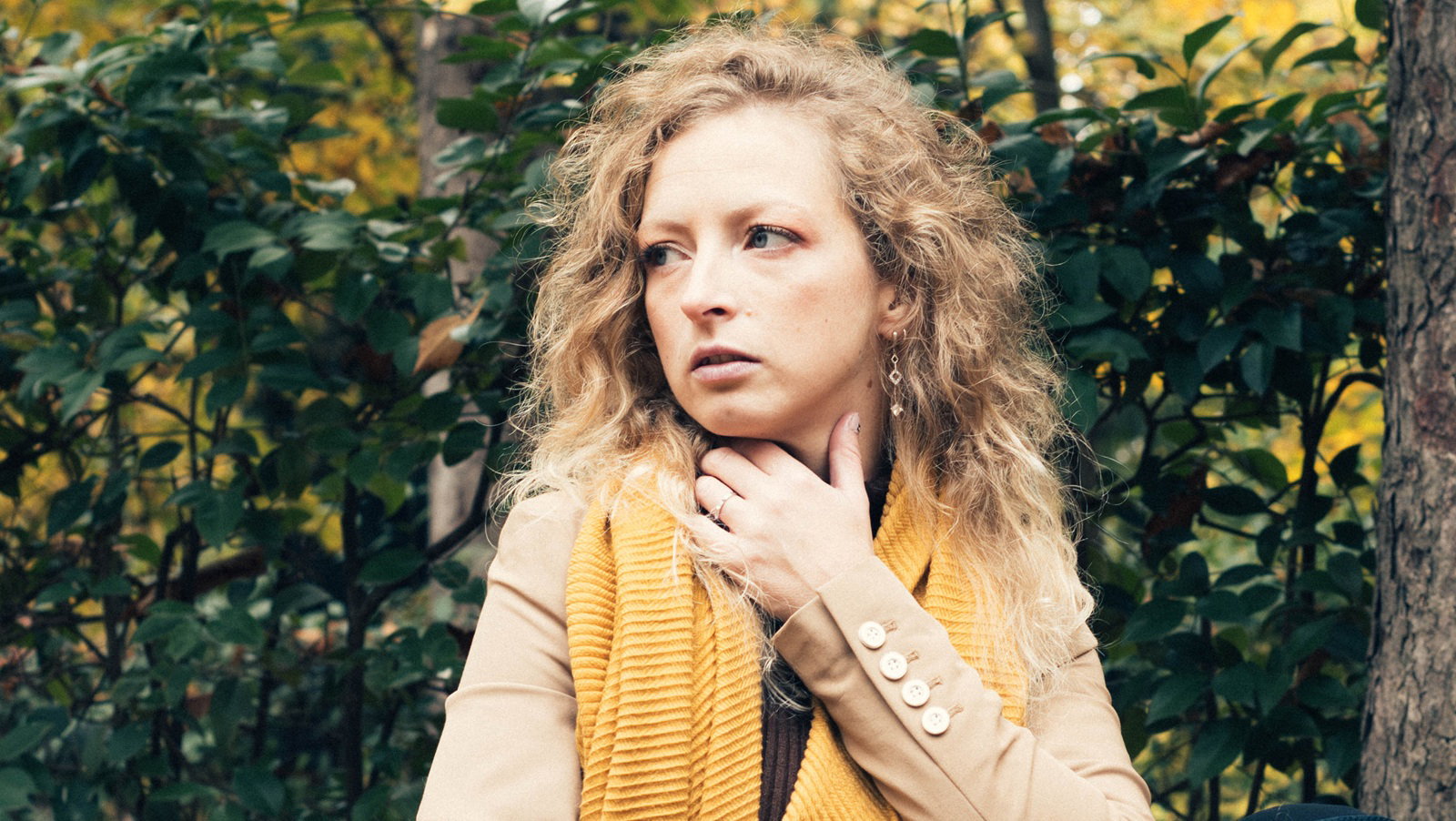 kobieta w wieku 30 plus z kręconymi blond włosami siedzi na tle jesiennego pejzażu z wystraszoną miną