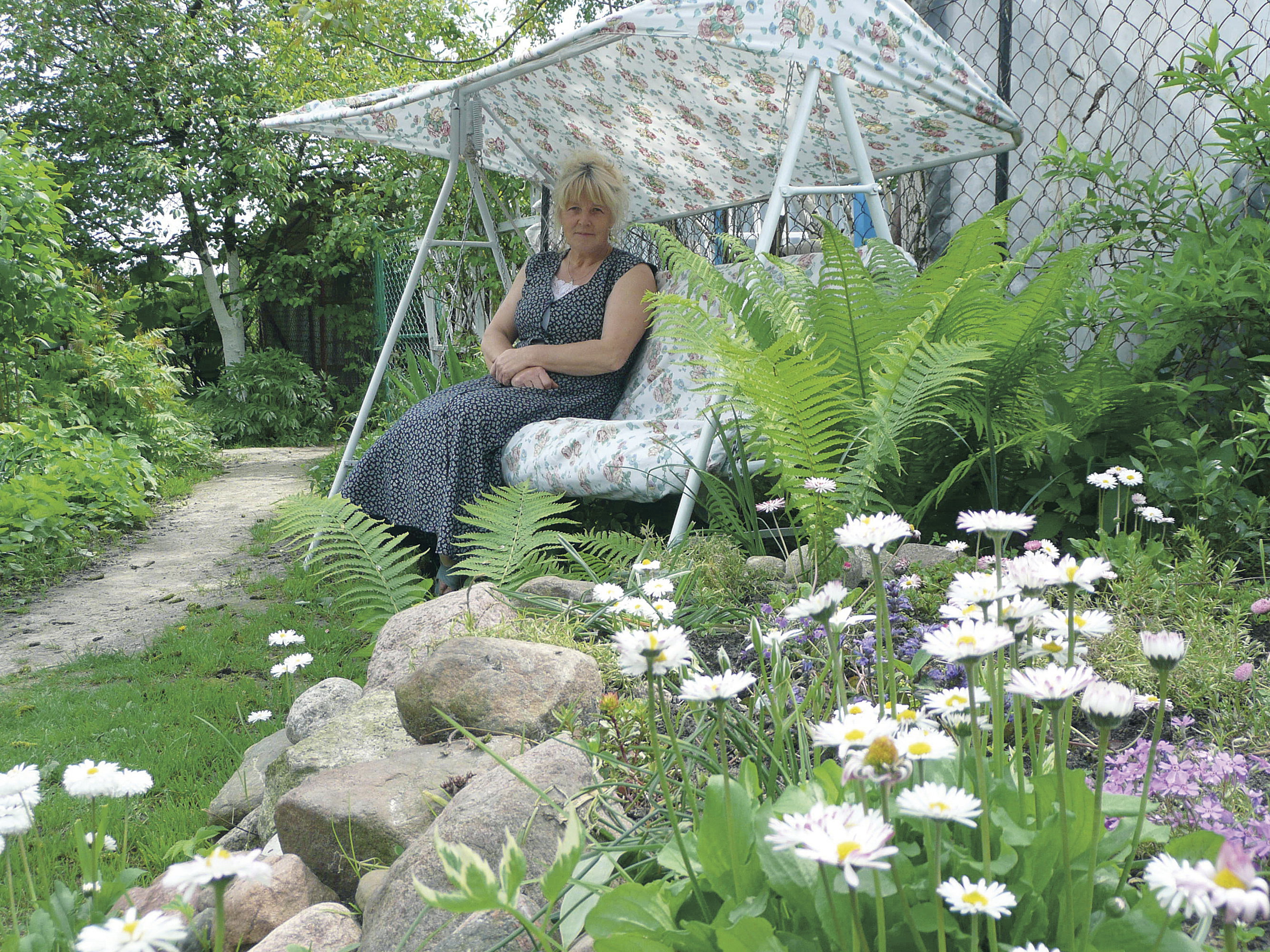 Bujana huśtawka ma jasne, kwieciste obicie, dzięki czemu nie wyróżnia się zbyt mocno na tle ogrodowej scenerii