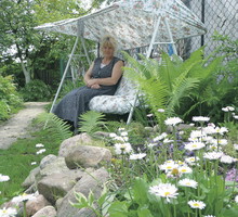 Bujana huśtawka ma jasne, kwieciste obicie, dzięki czemu nie wyróżnia się zbyt mocno na tle ogrodowej scenerii