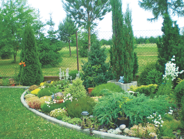 Rabatę o przyjaznym, okrągłym kształcie wypełniają rosnące bujnie gatunki traw, kwiatów i krzewów