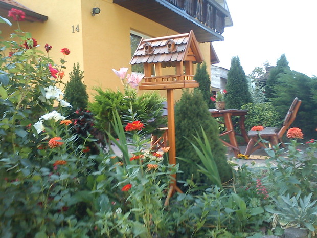 karmnik otoczony różami i liliami, w oddali meble ogrodowe