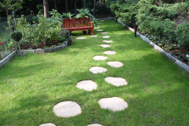 widok ze schodków tarasu na ogródek. Kamienne deptaki prowadzą do ławeczki i furtki na końcu ogródka. Trawa  jest tegoroczna, więc sądzę, że z każdym miesiącem będzie bujniejsza.