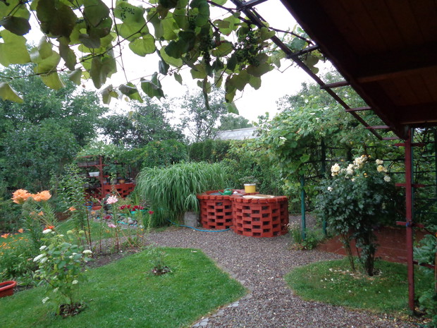 W jednej linii ustawione; kompostownik, oczko wodne, studnia z grillem i miejsce do wypoczynku. Zdjęcie po deszczu.