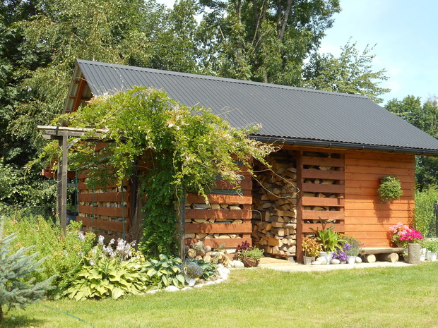 drewutnia ozdobiona kwiatami w donicach oraz pergolą po której pnie się Glicynia