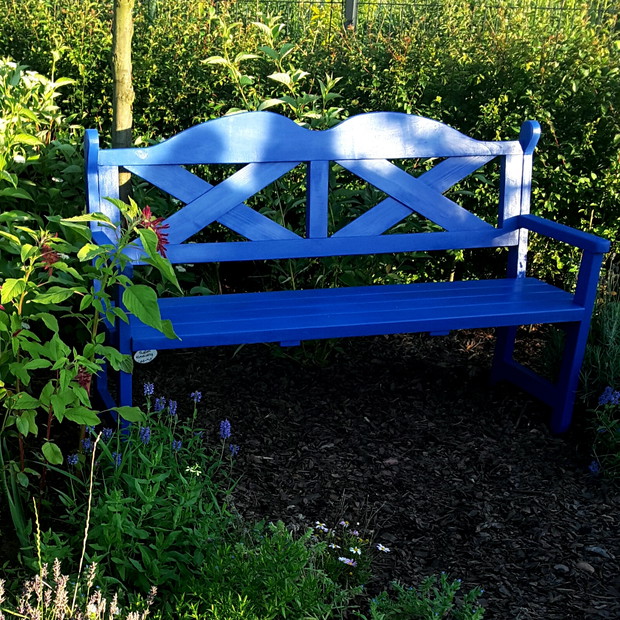 Niebieska ławka na końcu ogrodu. Siedząc na niej można oglądać całą rabatę bylinową wokół zelonej polany i zachód słońca.