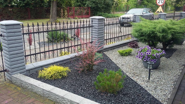 Przed domem postawiliśmy na czystość, uniwersalność i elegancję - miniaturowe rośliny rosną w kamieniach, kolorystyka czarno-szara, pasująca do elewacji domu i płotu.