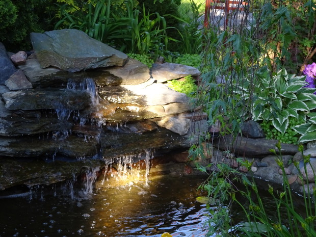 Zachodzące słońce w ogrodzie podświetla wodospad.