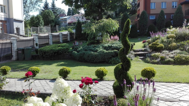 Widok na ogród, jezdnię, chodnik i blok mieszkalny. 