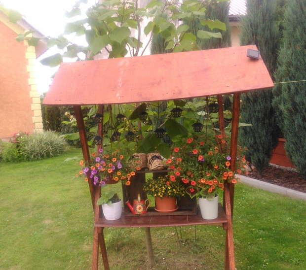 Drewniany stragan służy do ekspozycji kwiatów, oraz innych ozdób. Oświetla go solarne światełko.