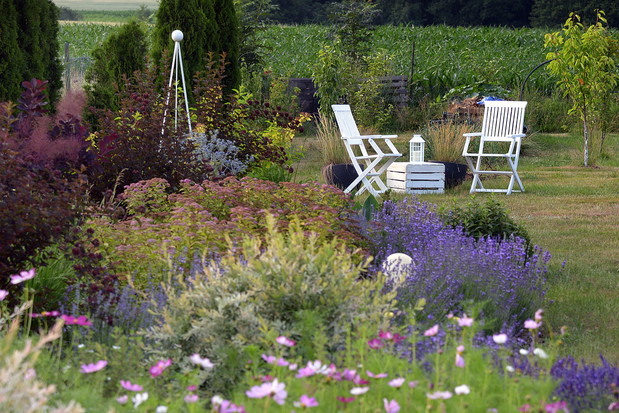Jedna z osi widokowych w ogrodzie. Od początku rabaty oko wędruje do białych mebli z latarenką na energię słoneczną. To zaproszenie dla gościa odwiedzającego, by spoczął i napił się herbaty z mięty, która rośnie w skrzyniach za pergolami.