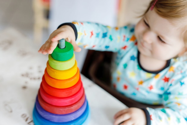 Adorable cute beautiful little baby girl playing with educational wooden rainbow toy pyramid