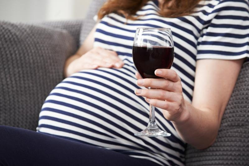 Kobieta w ciąży siedzi na kanapie z kieliszkiem wina