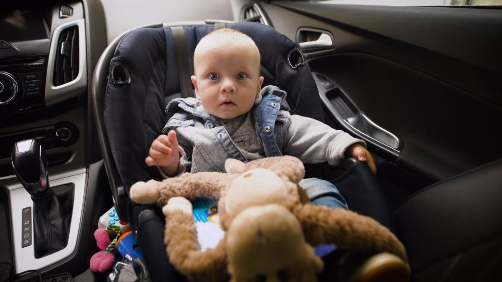 Zdziwione niemowlę siedzi w samochodzie w foteliku