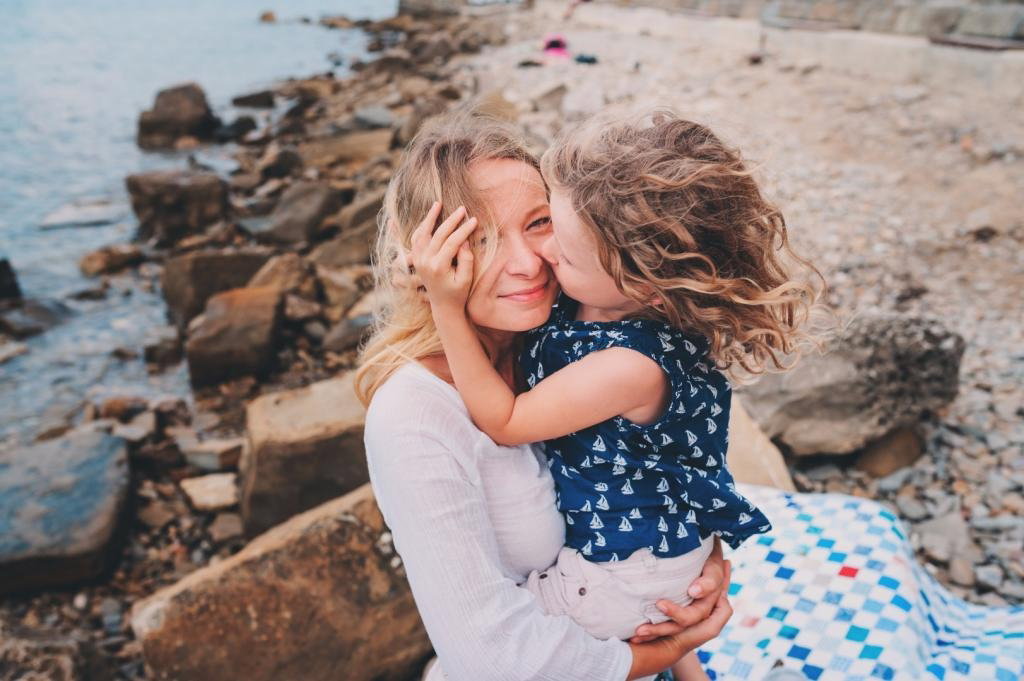 Uśmiechnięta mama przytula na plaży córeczkę