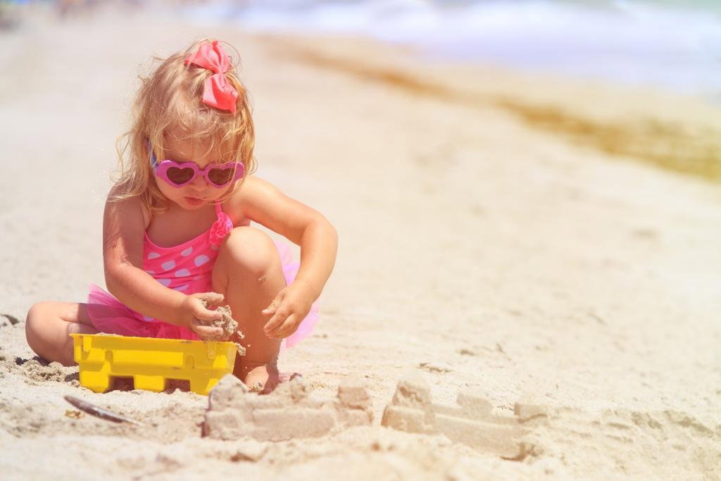 Dziewczynka w okularach przeciwsłonecznych bawi się sama na plaży