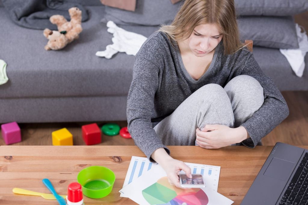 Zmęczona mama pracuje pośród zabawek porozrzucanych po pokoju