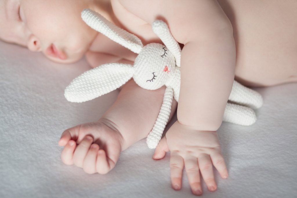 Niemowlę śpi w łóżeczku, przytulając pluszowego króliczka