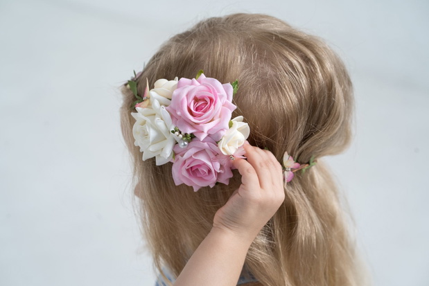 Litte blond girl with a flower crown. Side view, no face, one hand correcting head piece, on the white background, white and pink roses in her hair.